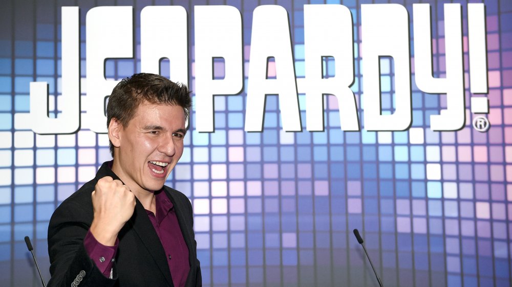 A photograph of James Holzhauer in front of the Jeopardy! logo