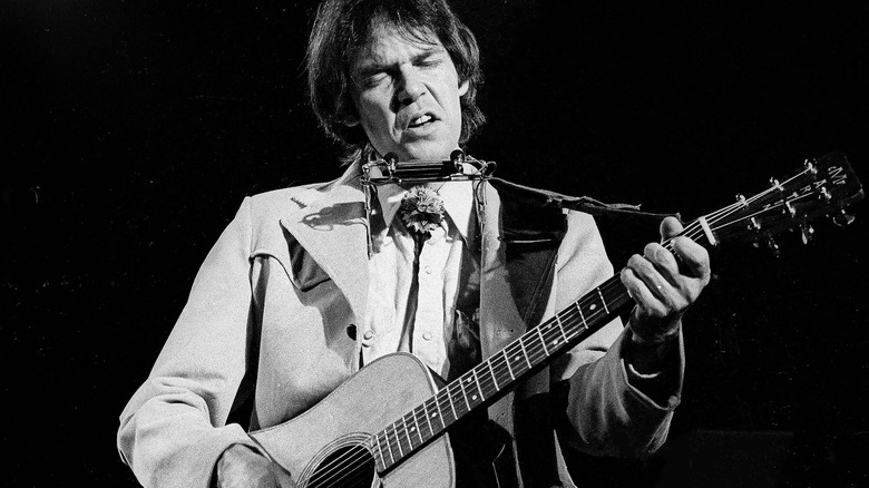 Neil Young performs with guitar and harmonica