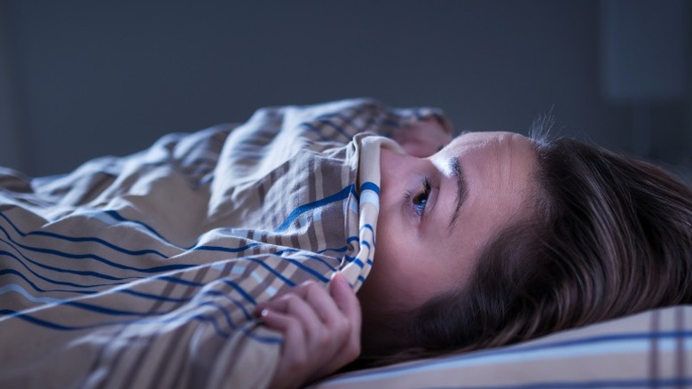 scared woman hiding under blanket