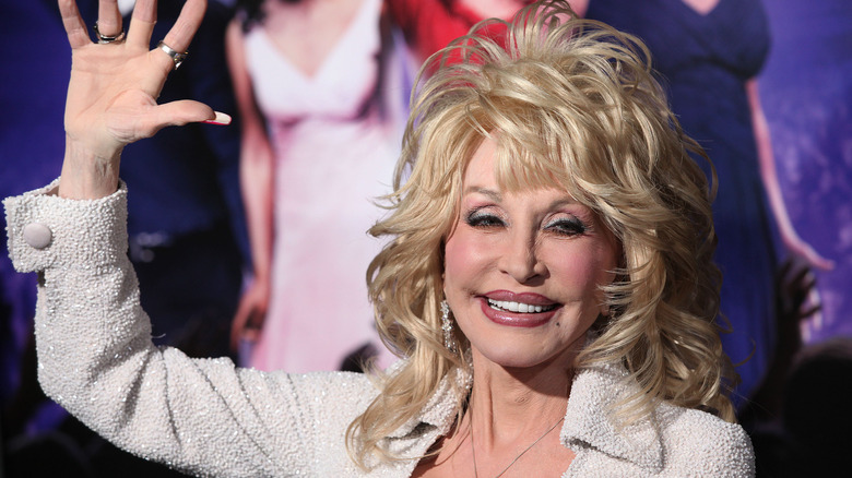 Smiling Dolly Parton waving a hand