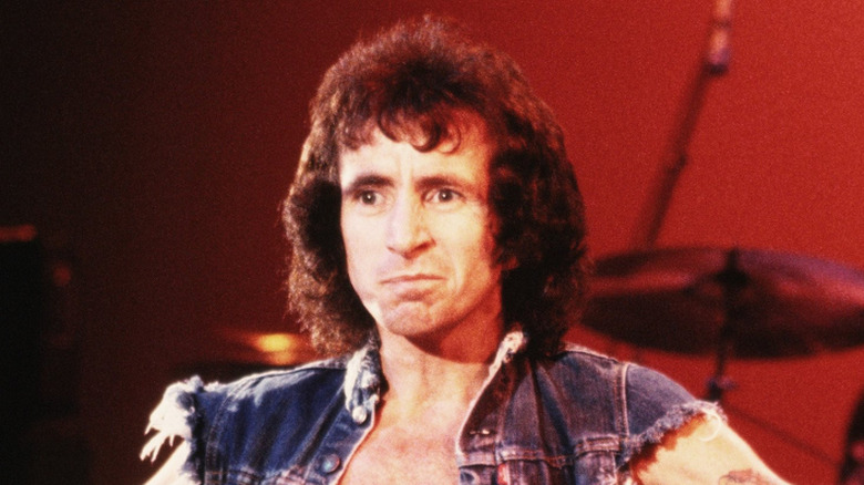 bon scott onstage smirking in denim vest