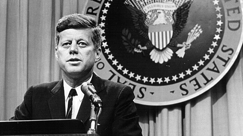 John F. Kennedy standing in front of the Presidential Seal