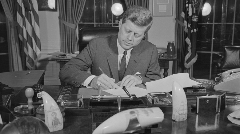 John F. Kennedy signing a paper in his office