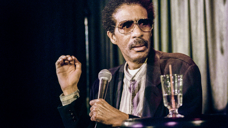 Richard Pryor seated holding microphone