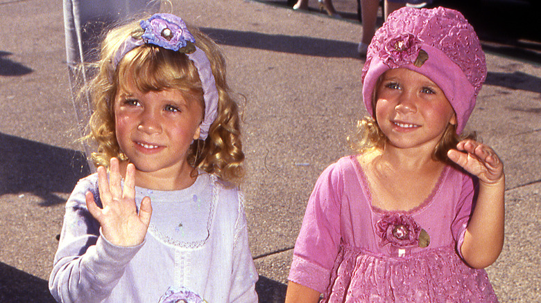 Smiling Mary-Kate and Ashley Olsen dressed up and waving