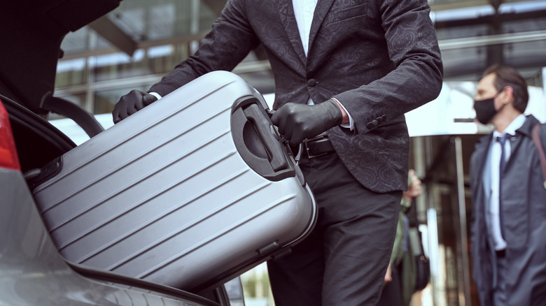 Man putting gray suitcase in trunk