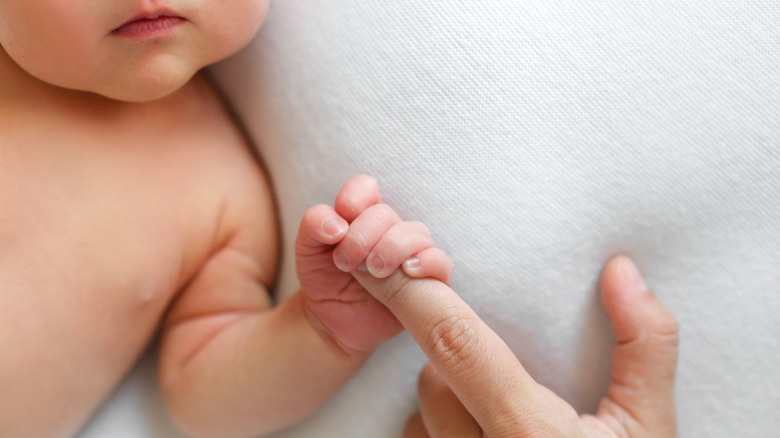 Newborn baby holding adult's finger