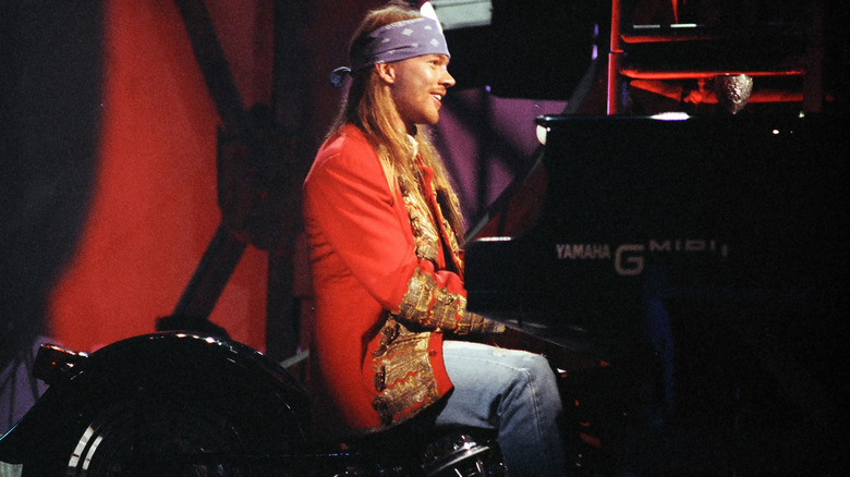 Axl Rose smiling red jacket sitting piano