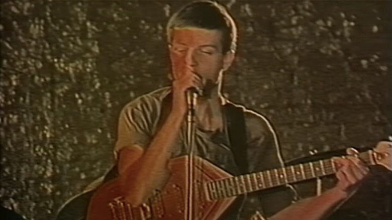 Ian Curtis singing, guitar in hand