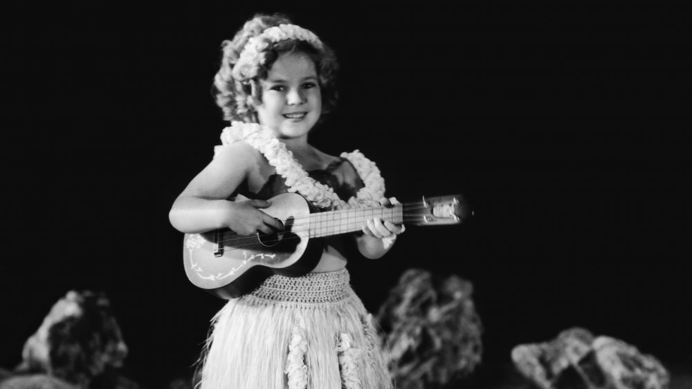 Shirley Temple wearing a grass skirt and playing a ukulele in a promotional portrait for the musical 'Captain January', directed by David Butler, 1936.