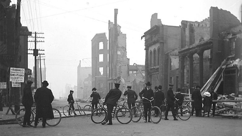 people on bicycles in front of burned buildings