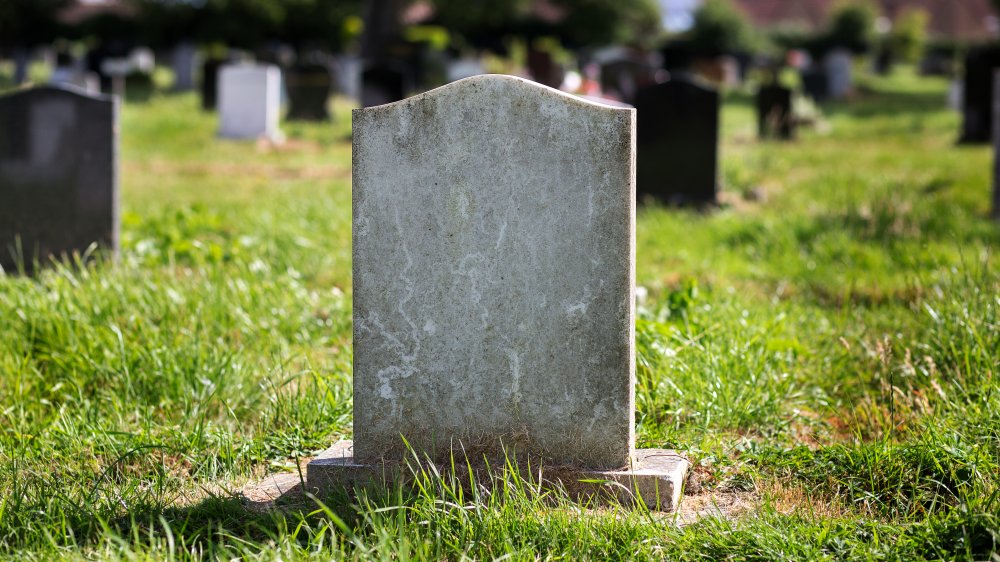 Blank gravestone with other graves and trees in background.