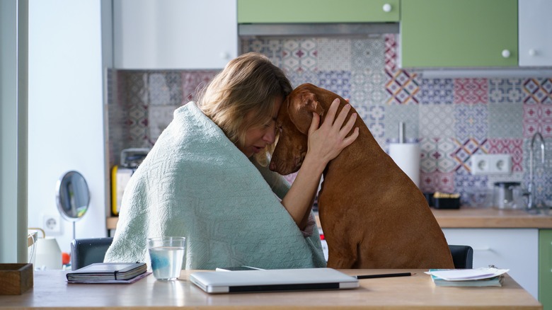 Sad woman comforted by her dog in the kitchen