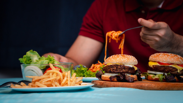 man eating spaghetti and hamburgers