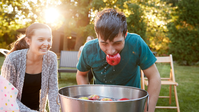 One person apple bobbing outdoors while another laughs