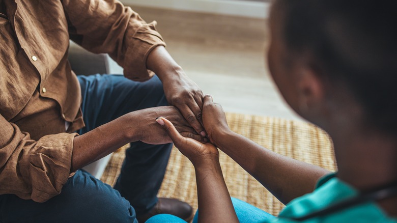 Close-up of Black home caregiver and senior person holding hands