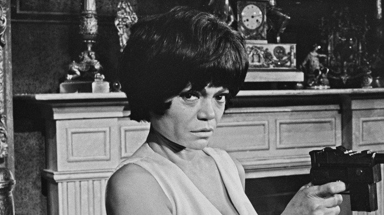 Eartha Kitt staring into the camera on a film set holding a pistol