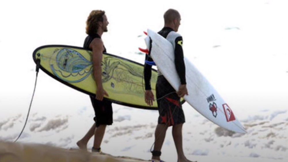 Eddie Vedder on beach carrying surfboard