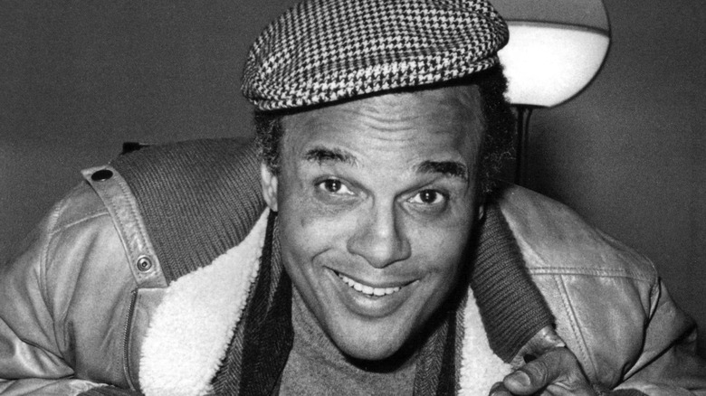 Harry Belafonte smiling goofily in a hat and leather jacket