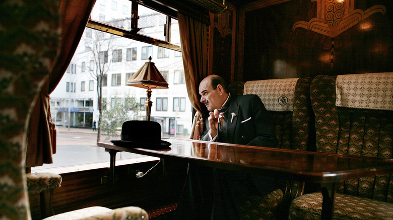 actor dressed as Poirot sitting in an original car from the Orient Express train