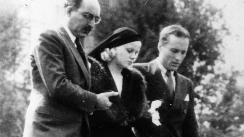 Jean Harlow assisted by two men walking to Paul Bern's funeral