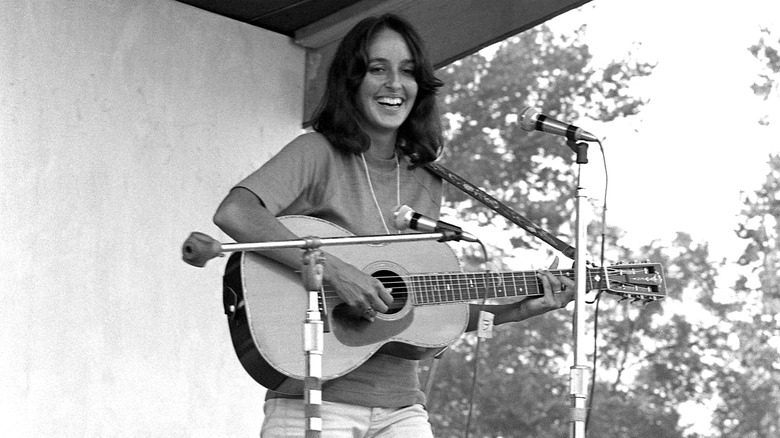 Joan Baez performing outdoors with trees in the background