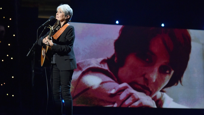 Joan Baez on stage in front of ascreen and her photo