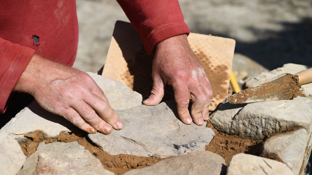 man setting stone into pattern with other stones and mud