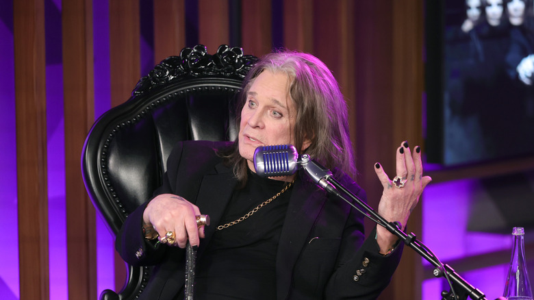 Ozzy Osbourne sitting in a fancy black chair and speaking in a microphone