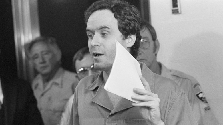 Ted Bundy holds a piece of paper as police officers stand behind him