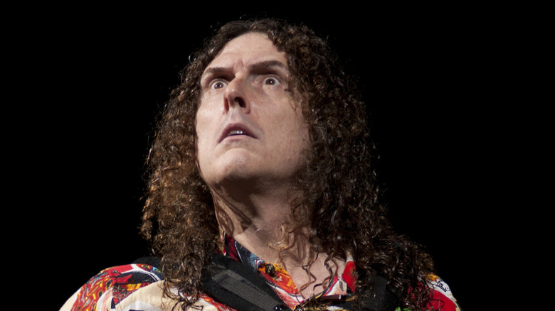 Weird Al Yankovic looks up with mock seriousness while playing accordion on stage.