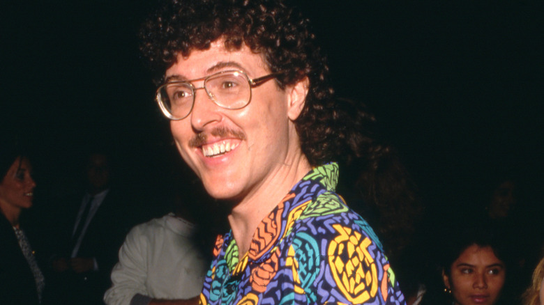 weird al yankovic smiling in glasses and print shirt looking off