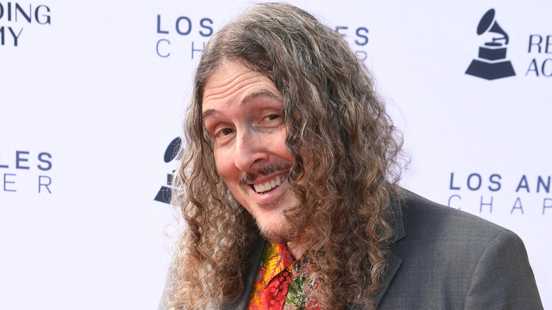 Weird Al Yankovic is smiling while wearing a gray blazer.