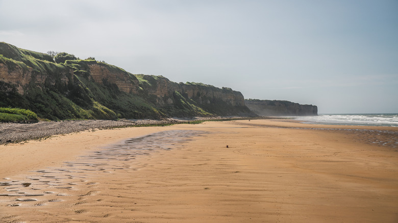 Modern view of Omaha Beach in Normandy, France with ocean to the right and cliffs to the left.