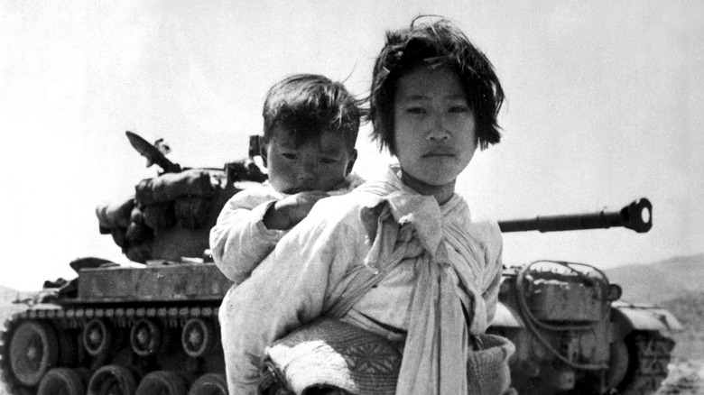 Little Korean girl holding boy on back with tank in the background