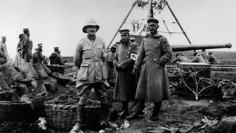 A British officer with two of his Japanese counterparts beside a camouflaged heavy gun in 1914 Tsingtau, China