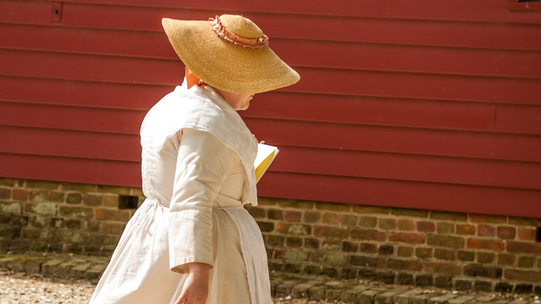 Woman dressed in colonial period clothing walking in Colonial Williamsburg, Virginia.