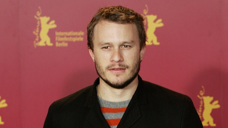 Heath Ledger black jacket red background at event