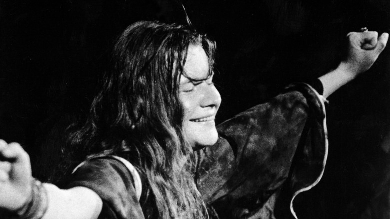 Janis Joplin with her eyes closed, smiling while performing onstage