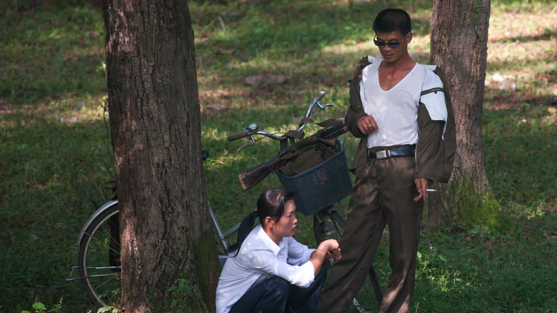 North Korean man holding a cigarette looking down at his girlfriend