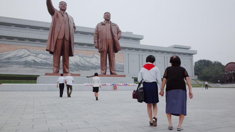 North Koreans walking under large statues