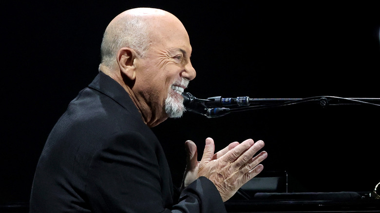 billy joel in suit smiling sat at piano