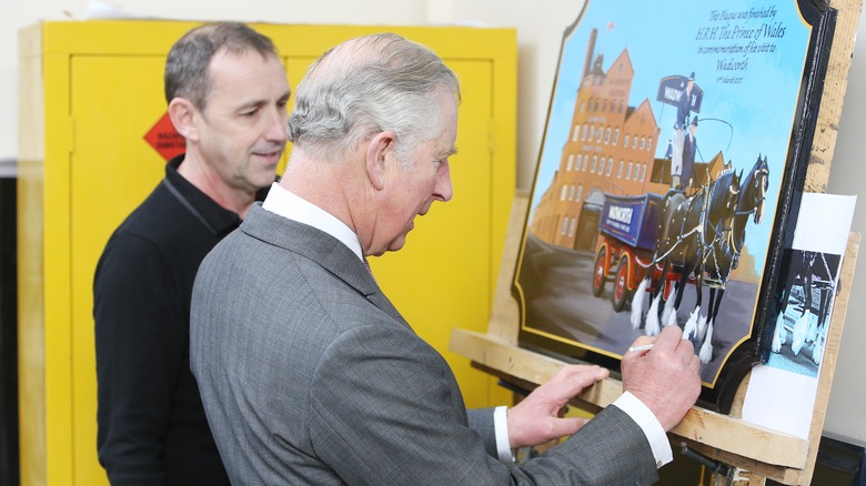 Prince Charles signs a plaque smiling