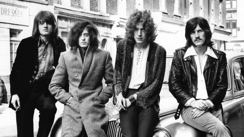 Led Zeppelin's four members posing on hood of car in urban street