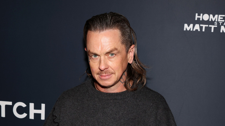 Long-haired Sid Wilson wearing a grey jumper and posing on the red carpet