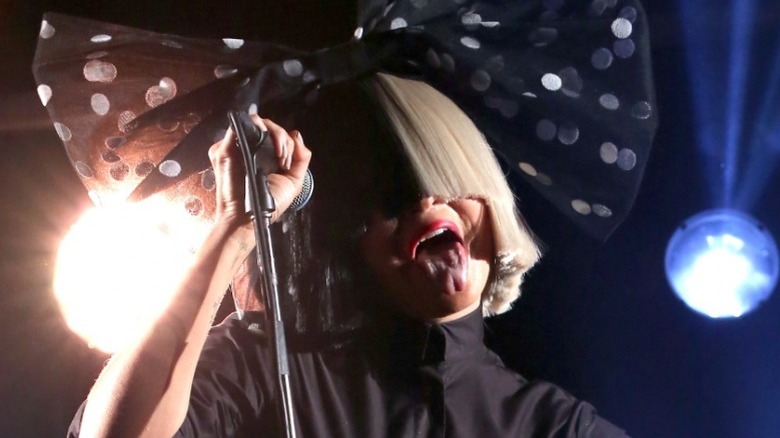 Sia sticking her tongue out while performing wearing a wig and bow