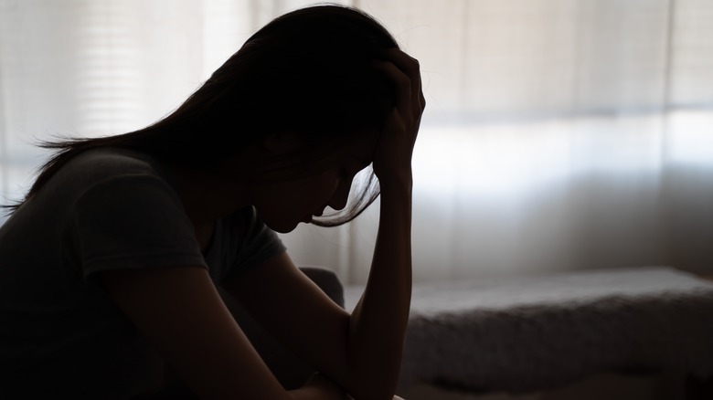 person with long hair sitting in a bed hold their head in their hands