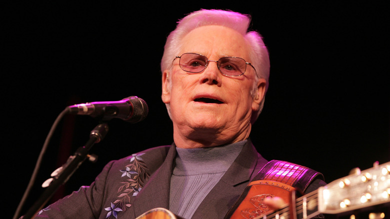 george jones playing guitar on stage and singing into microphone