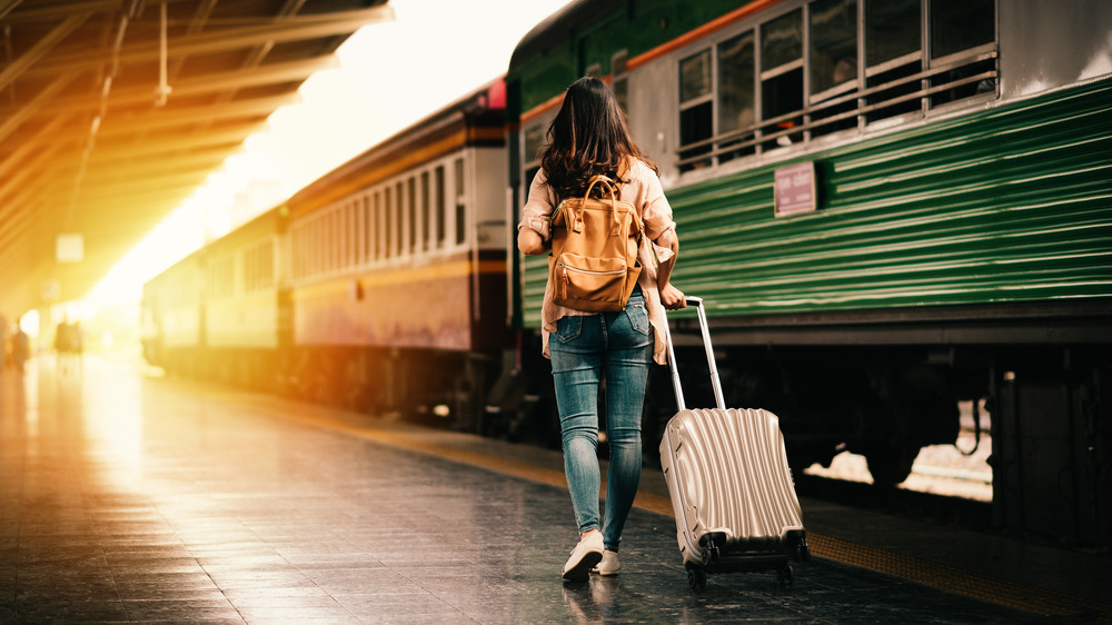 A photograph of a young woman pulling a suitcase through an airport.