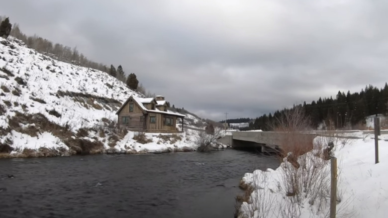 Old wooden building on steep river bank bridge snowy